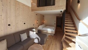 Un interior moderno con piso de madera, un sofá, una cama y una escalera.