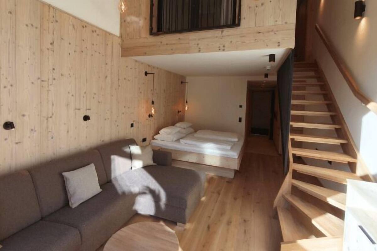 Un interior moderno con piso de madera, un sofá, una cama y una escalera.