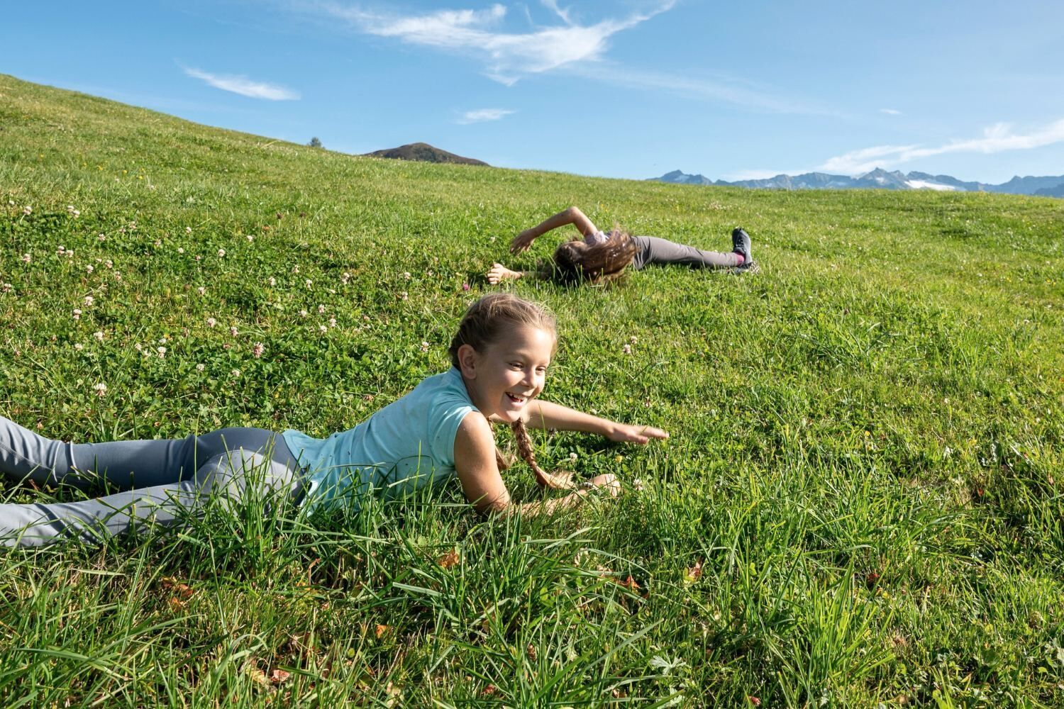Dos personas descansando sobre un campo cubierto de hierba, con una montaña al fondo.
