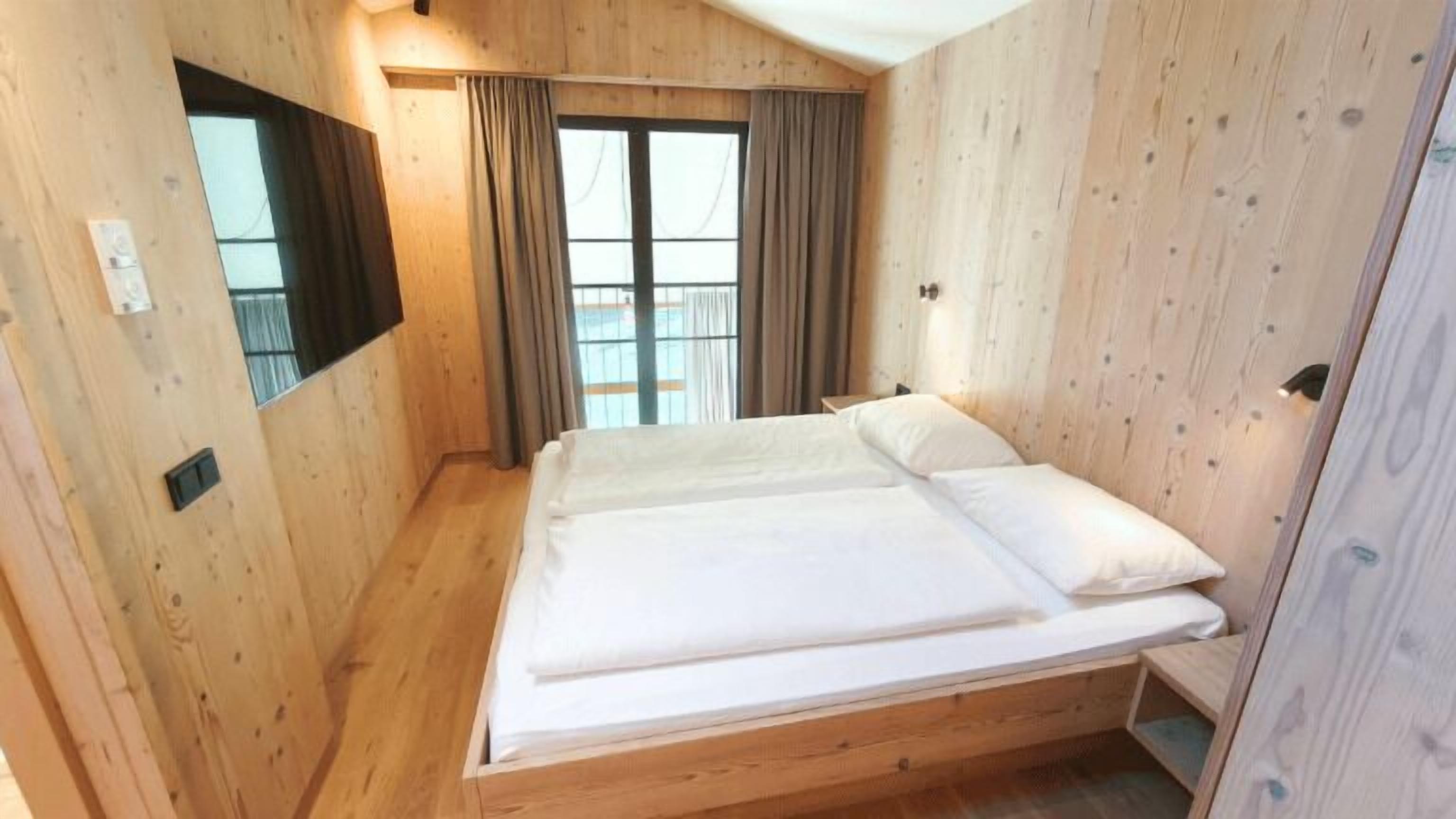 A wooden room with a bed, a window, and a curtain.