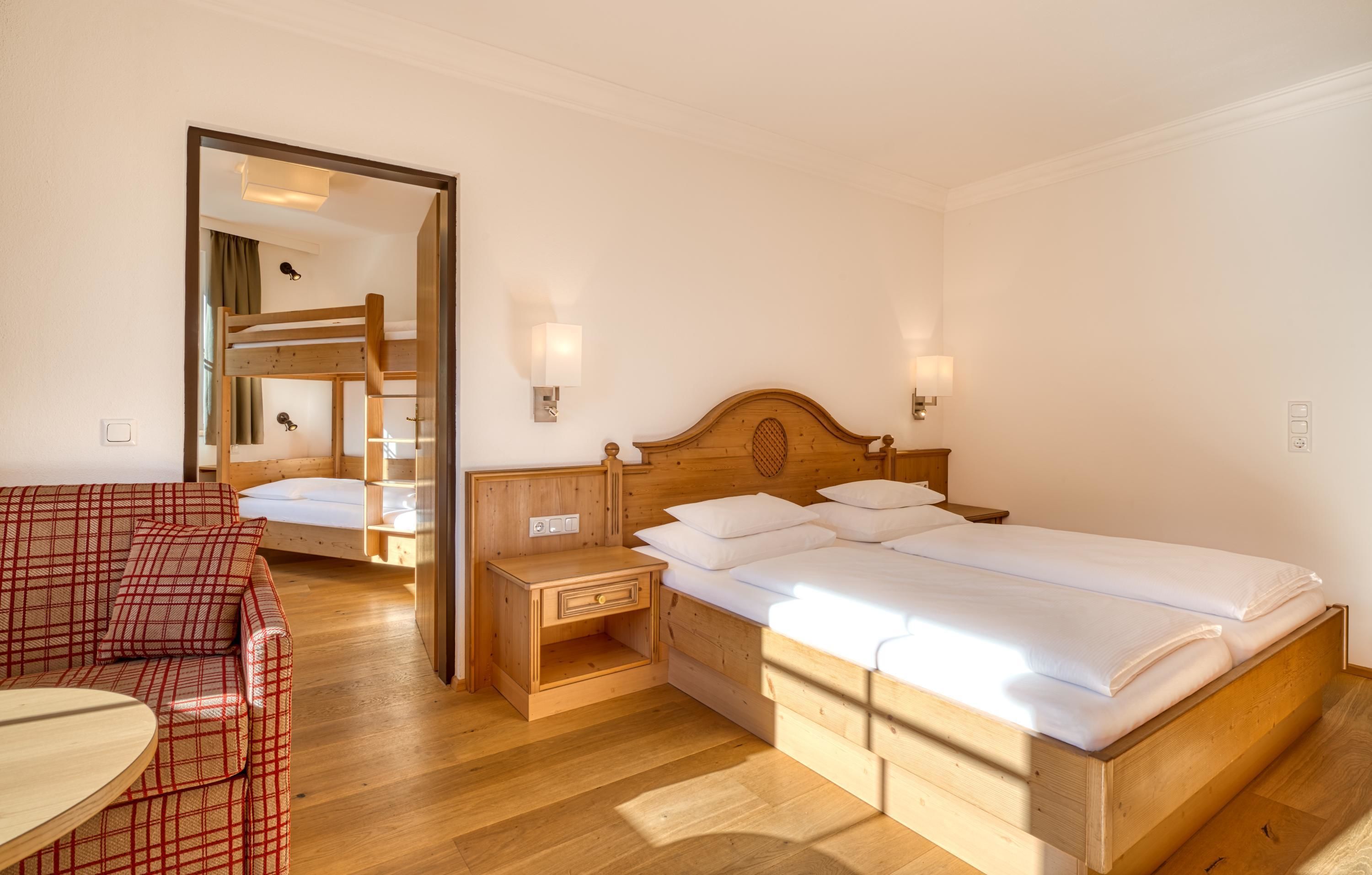 A bedroom with a wooden bed, a nightstand, a red plaid sofa, and a mirror.