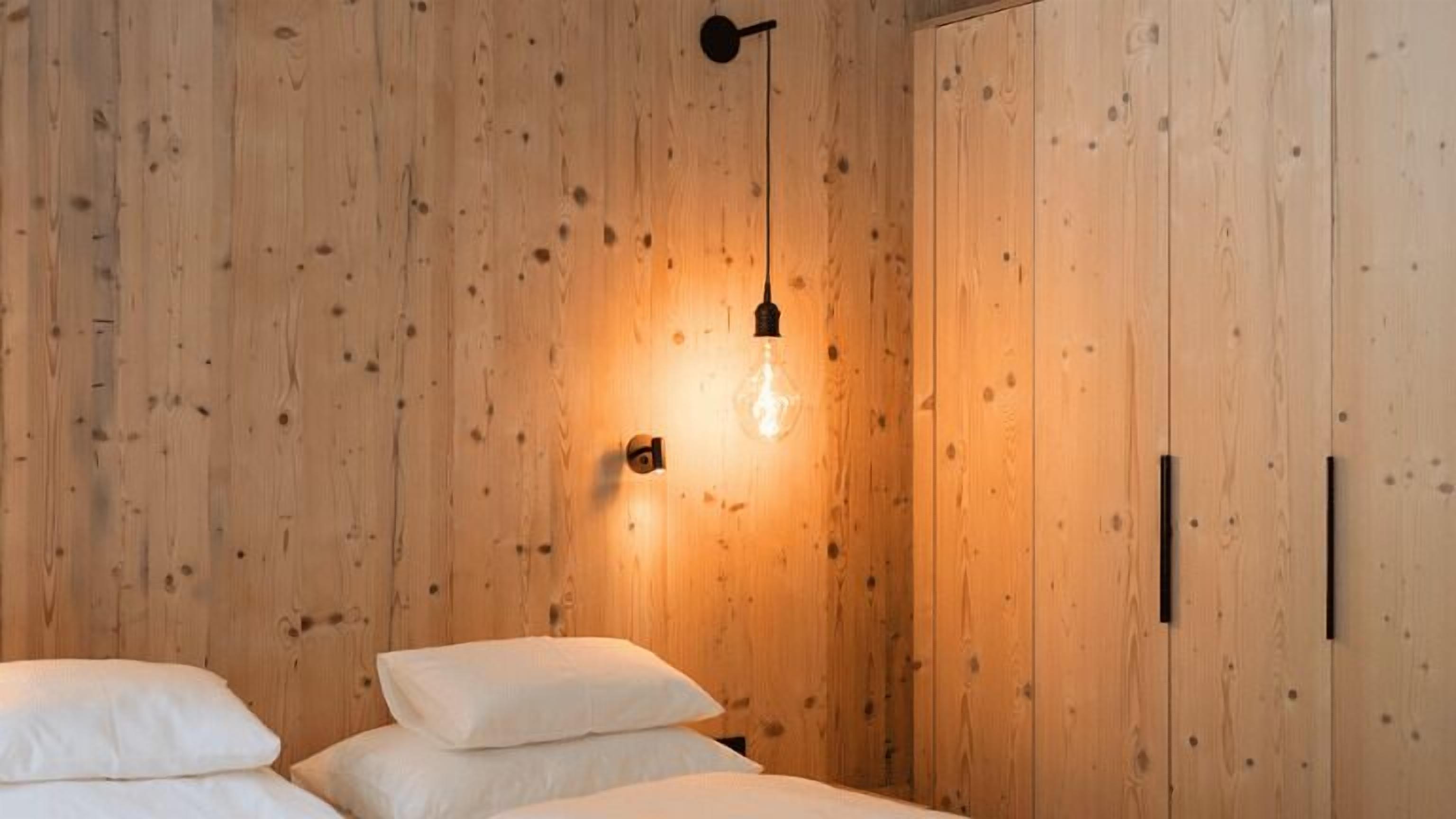 A wooden room with a bed, a hanging light fixture, and a wardrobe.