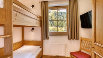 Een kamer met een stapelbed, een enkel bed, een stoel, een televisie en een raam met gordijnen.