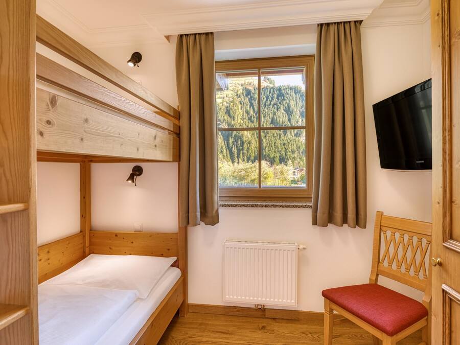 Een kamer met een stapelbed, een enkel bed, een stoel, een televisie en een raam met gordijnen.
