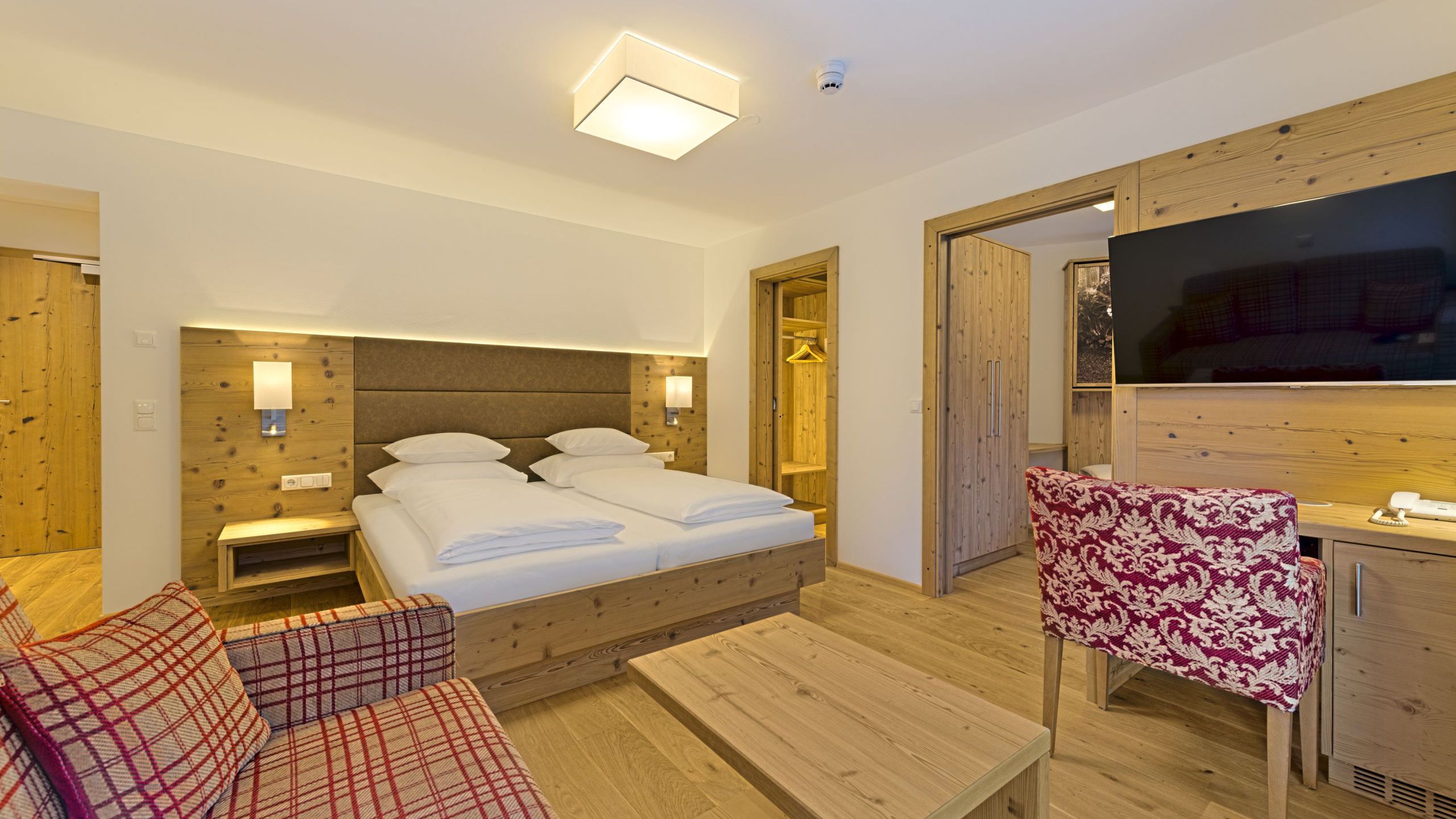 A hotel room with a wooden bed, a wooden desk, a TV, and a sofa.