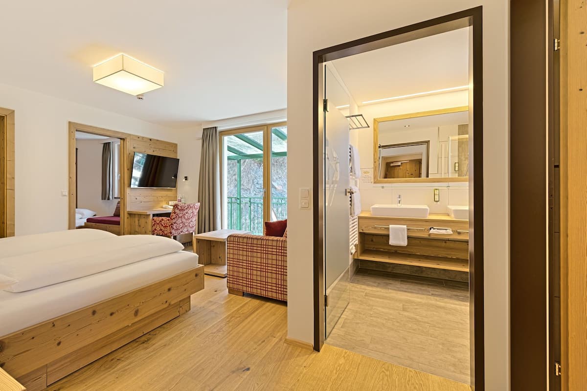 Una habitación de hotel moderna con suelo de madera, una cama grande, televisión y un balcón con vistas.