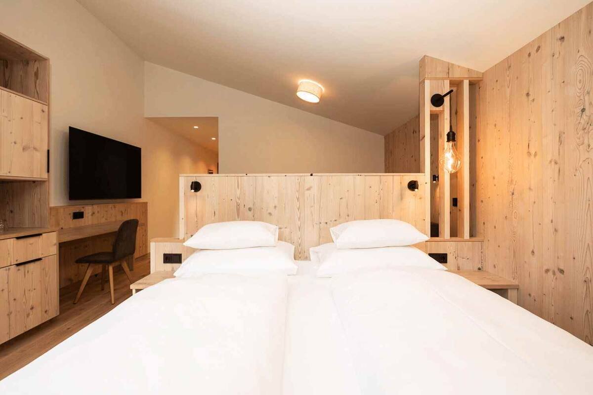 Un dormitorio moderno con dos camas, paredes de madera, un escritorio y un televisor.