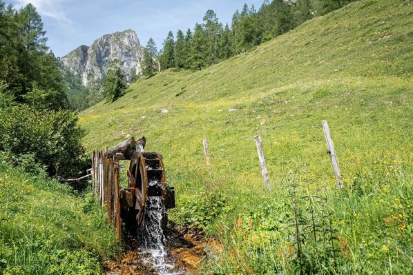 Un viejo pozo de agua rústico en un campo verde exuberante, con montañas al fondo.