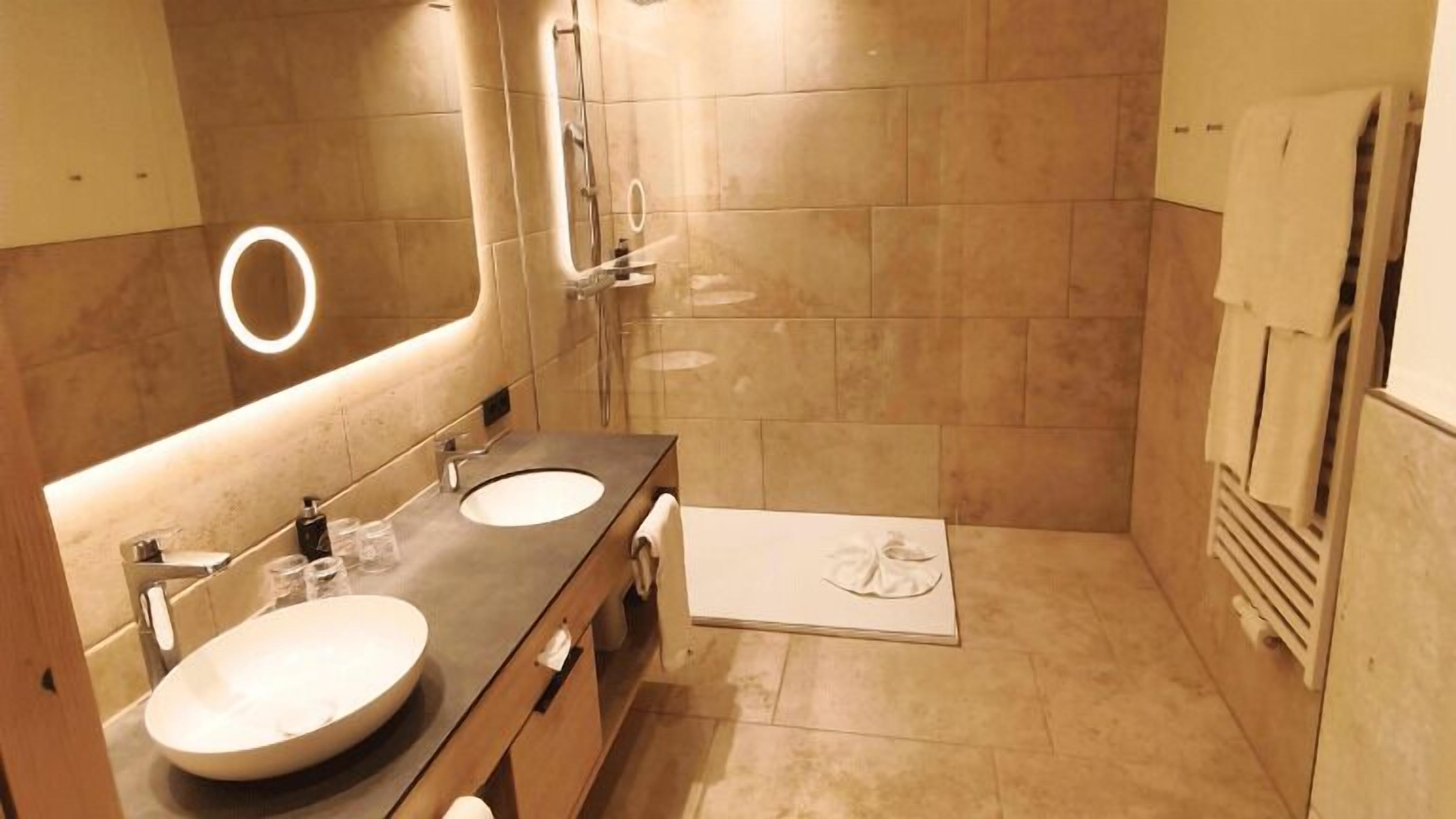Un baño moderno con dos lavamanos, un espejo grande y una ducha a ras de suelo.