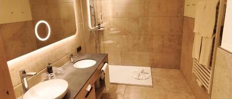 A modern bathroom with two sinks, a large mirror, and a walk-in shower.