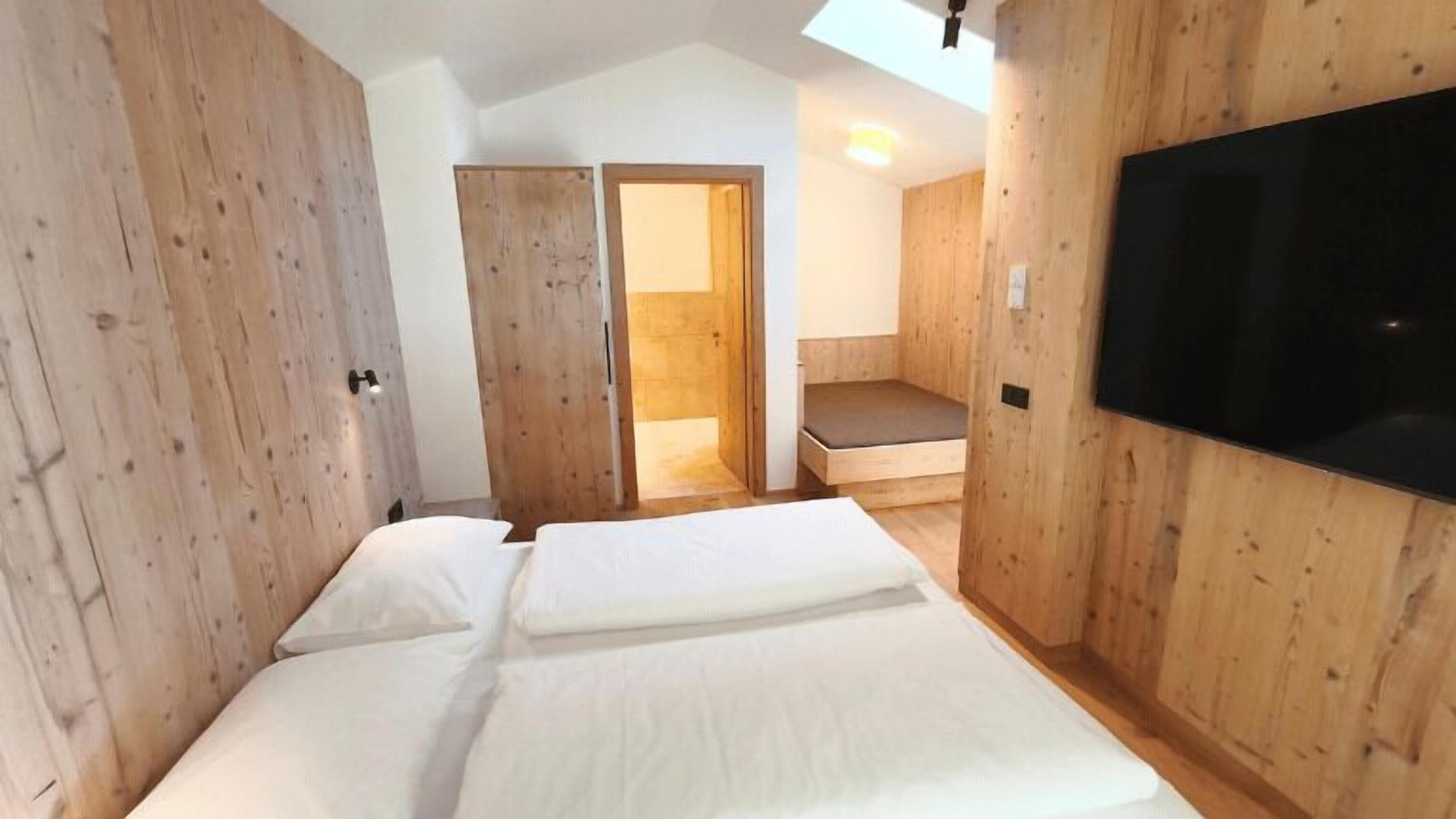 Un dormitorio con cama, paredes de madera, televisor y una escalera que lleva a un balcón.