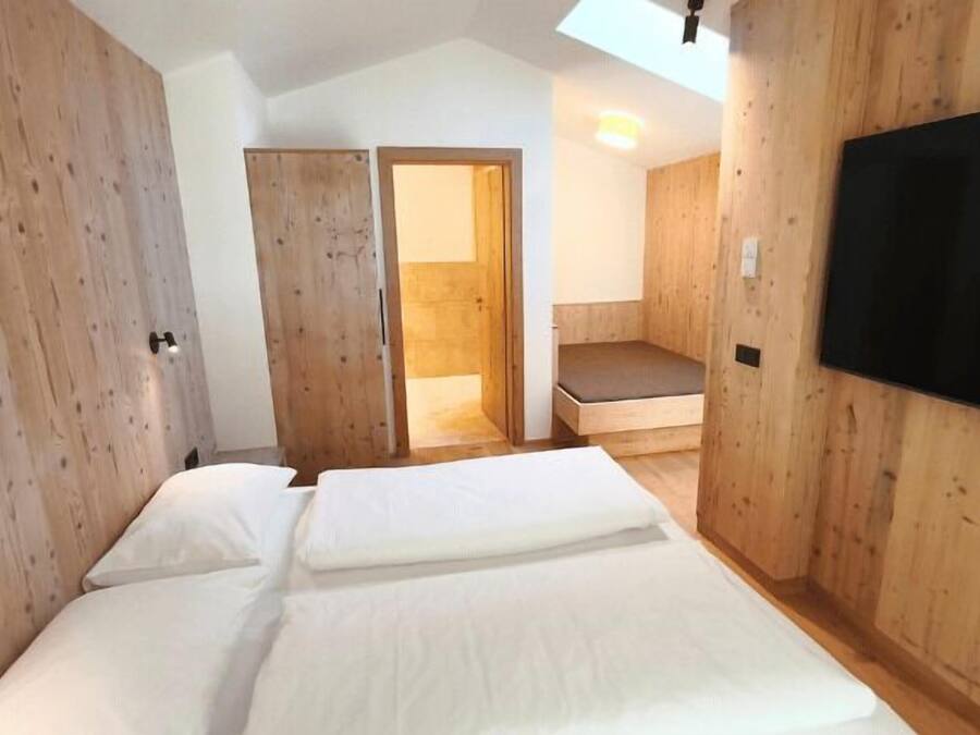 Un dormitorio con cama, paredes de madera, televisor y una escalera que lleva a un balcón.