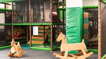 Zona de juegos con una estructura de red para escalar, un caballo balancín de madera y un tapete acolchado.