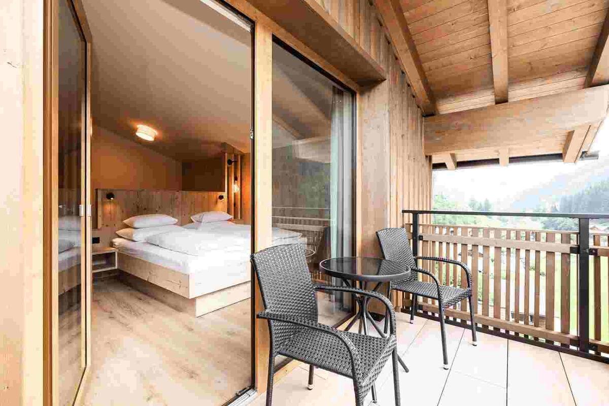 Un balcón de madera con una cama y dos sillones de mimbre.