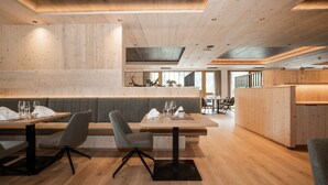 Un restaurante moderno con paredes y techo de madera, que cuenta con una larga mesa común con sillas y una zona de bar elevada.