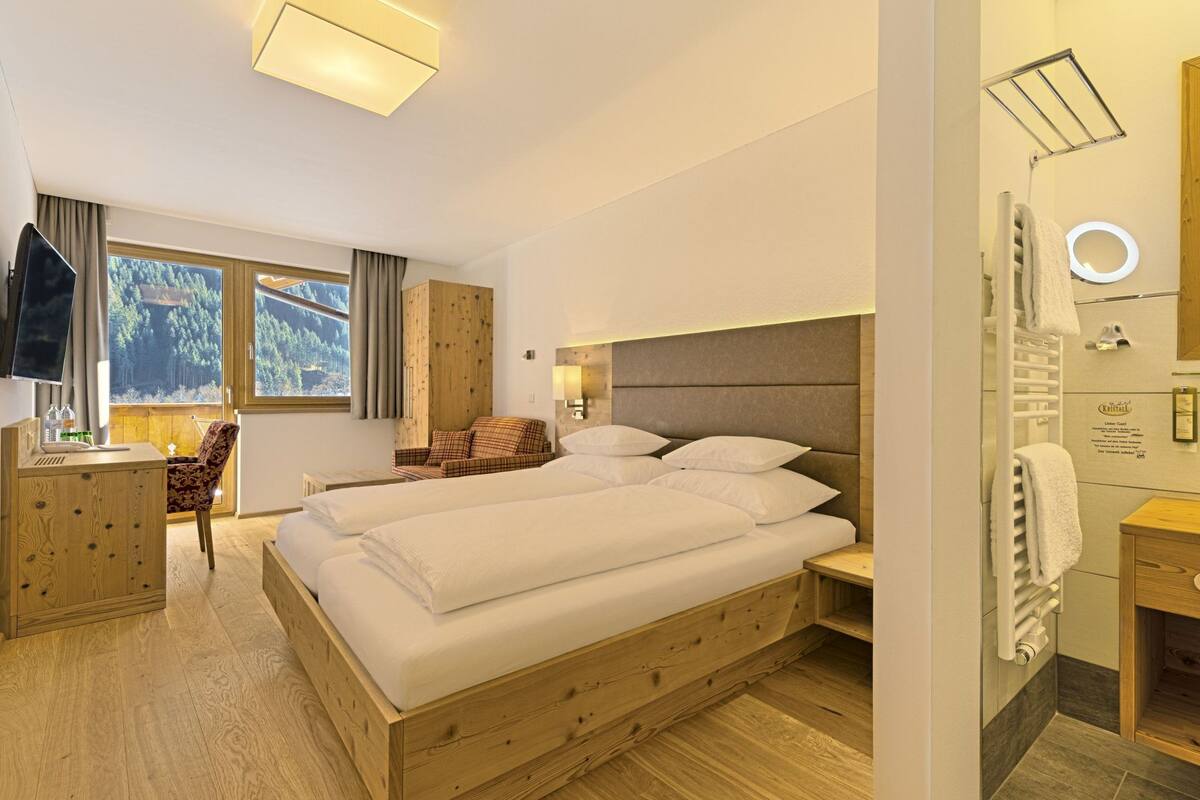 Habitación de hotel con una cama grande, un escritorio, una silla, un baño con espejo y vistas al exterior.