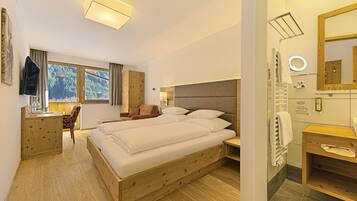 Habitación de hotel con una cama grande, un escritorio, una silla, un baño con espejo y vistas al exterior.