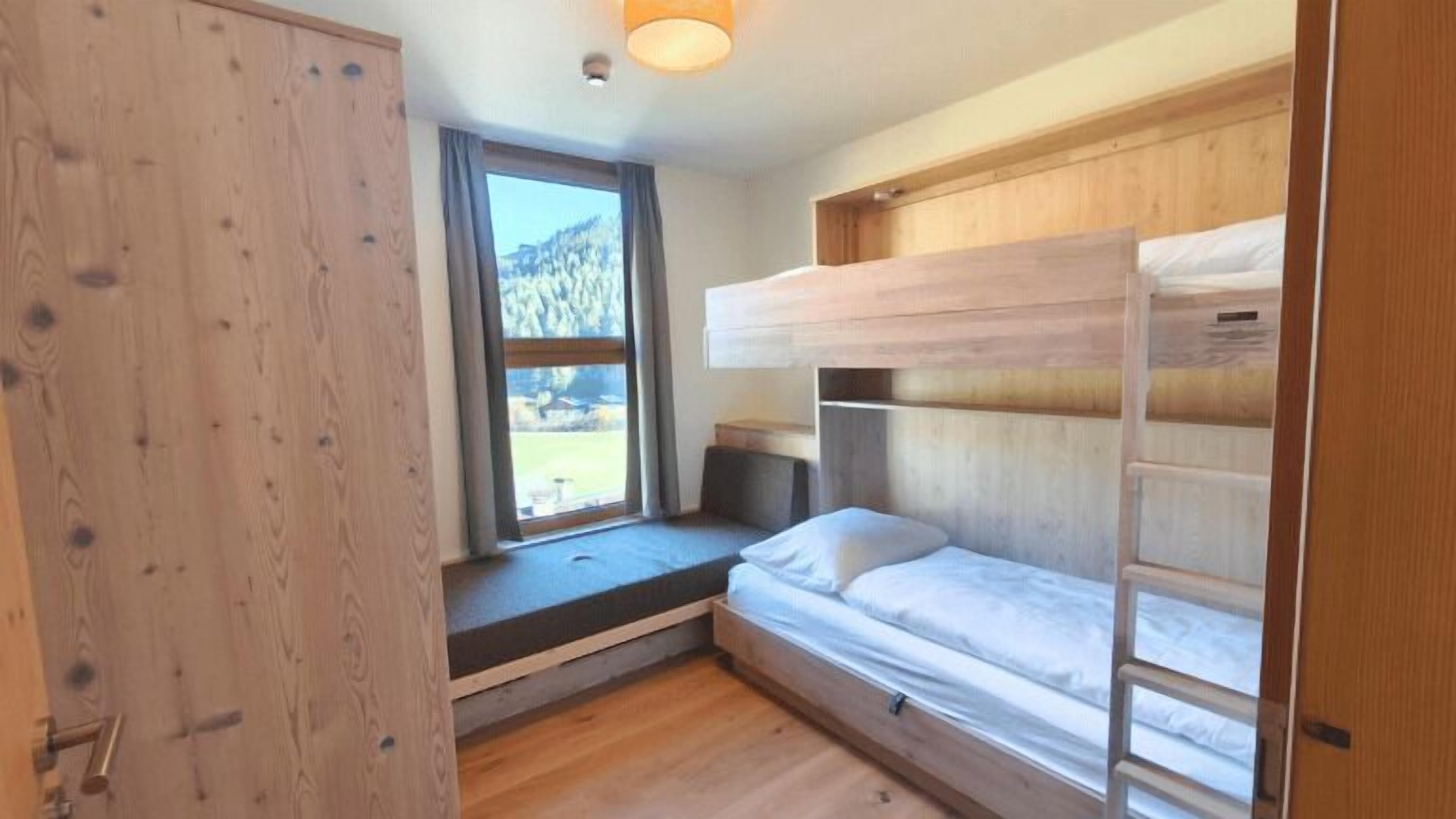 A compact room with a bunk bed, a window with a view of a mountain, and a wooden wardrobe.