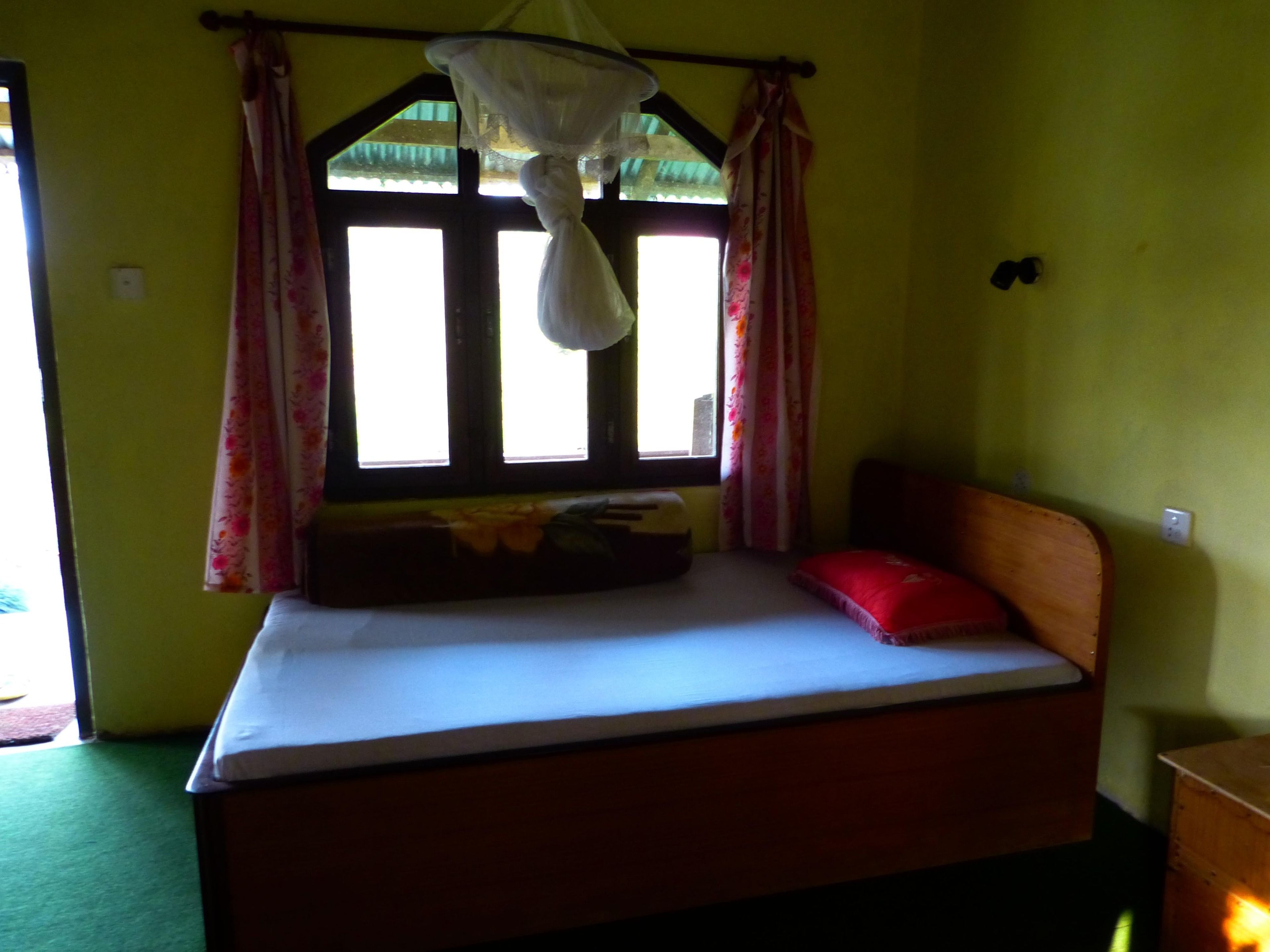 Una habitación con una cama, una ventana con cortinas y un mosquitero sobre la cama.