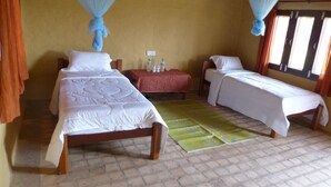 Una habitación con dos camas, una mesita con botellas de agua y una mosquitera.