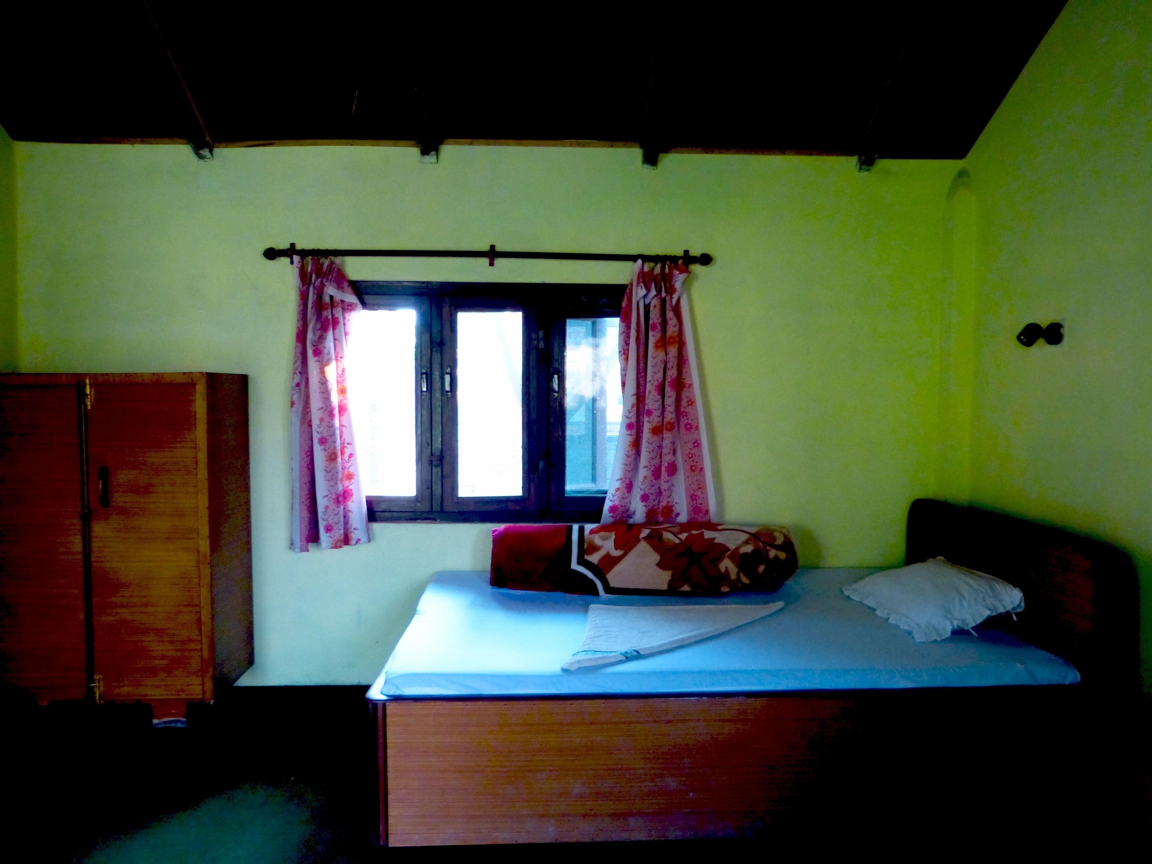 A room with a bed, a window with curtains, and a wardrobe.