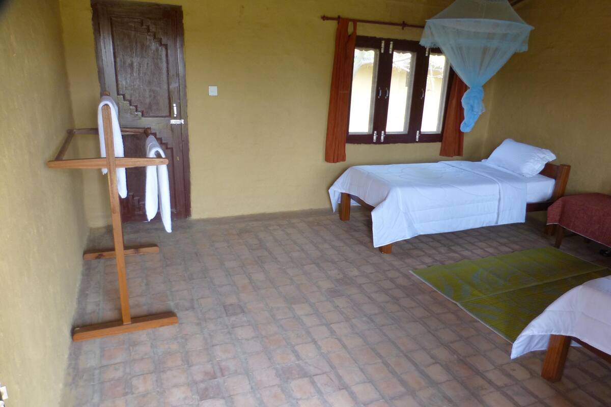 A room with two beds, a wooden chair, a small table, and a window with curtains.