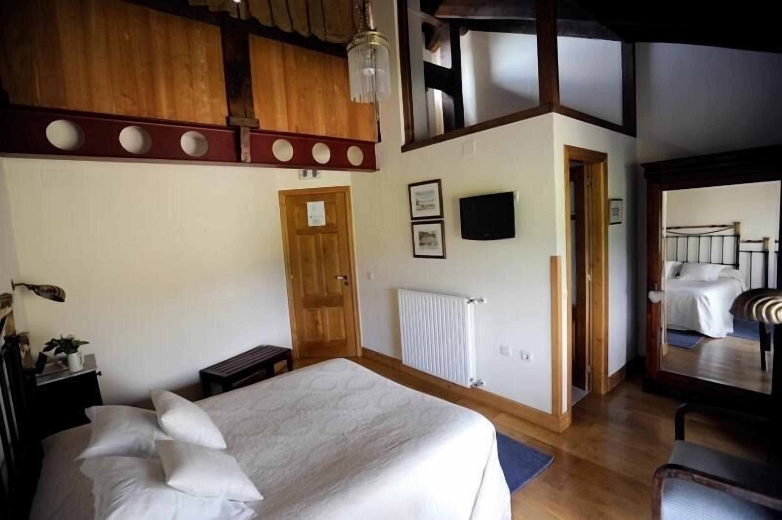 Un dormitorio con una cama grande, vigas de madera en el techo, un radiador y un espejo que refleja la cama.