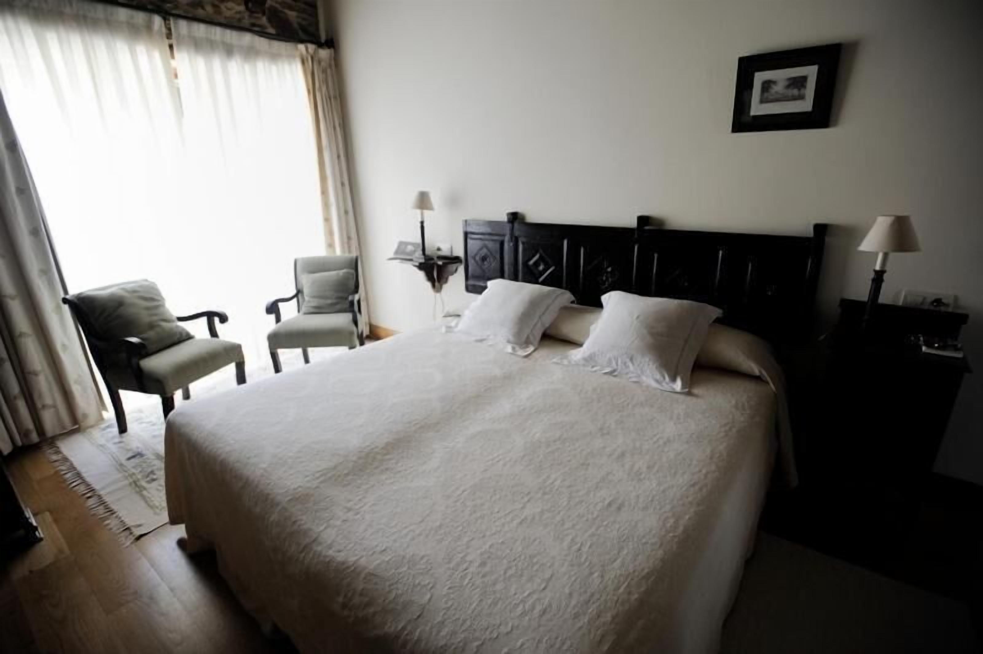 A neatly arranged hotel room with a large bed, two bedside tables, a chair, and a window with curtains.