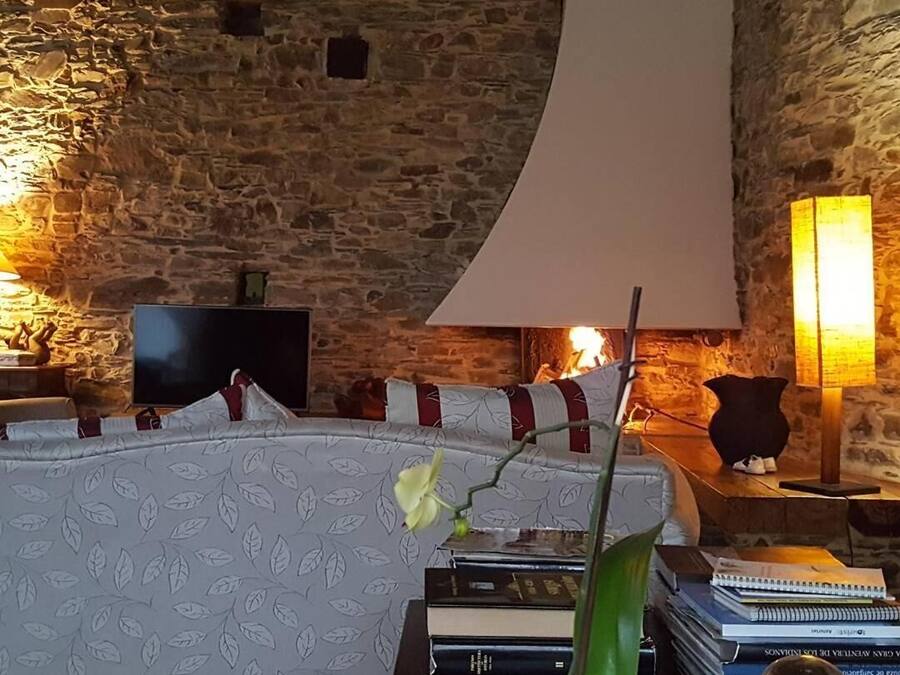 Une pièce chaleureuse avec un mur en pierre, un lit recouvert d’une literie à motifs, un téléviseur à écran plat, une grande lampe et des livres posés sur une table d’appoint.