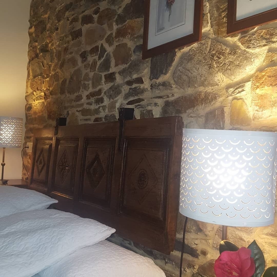 Pared de piedra, cabecera de madera y cama con ropa blanca.