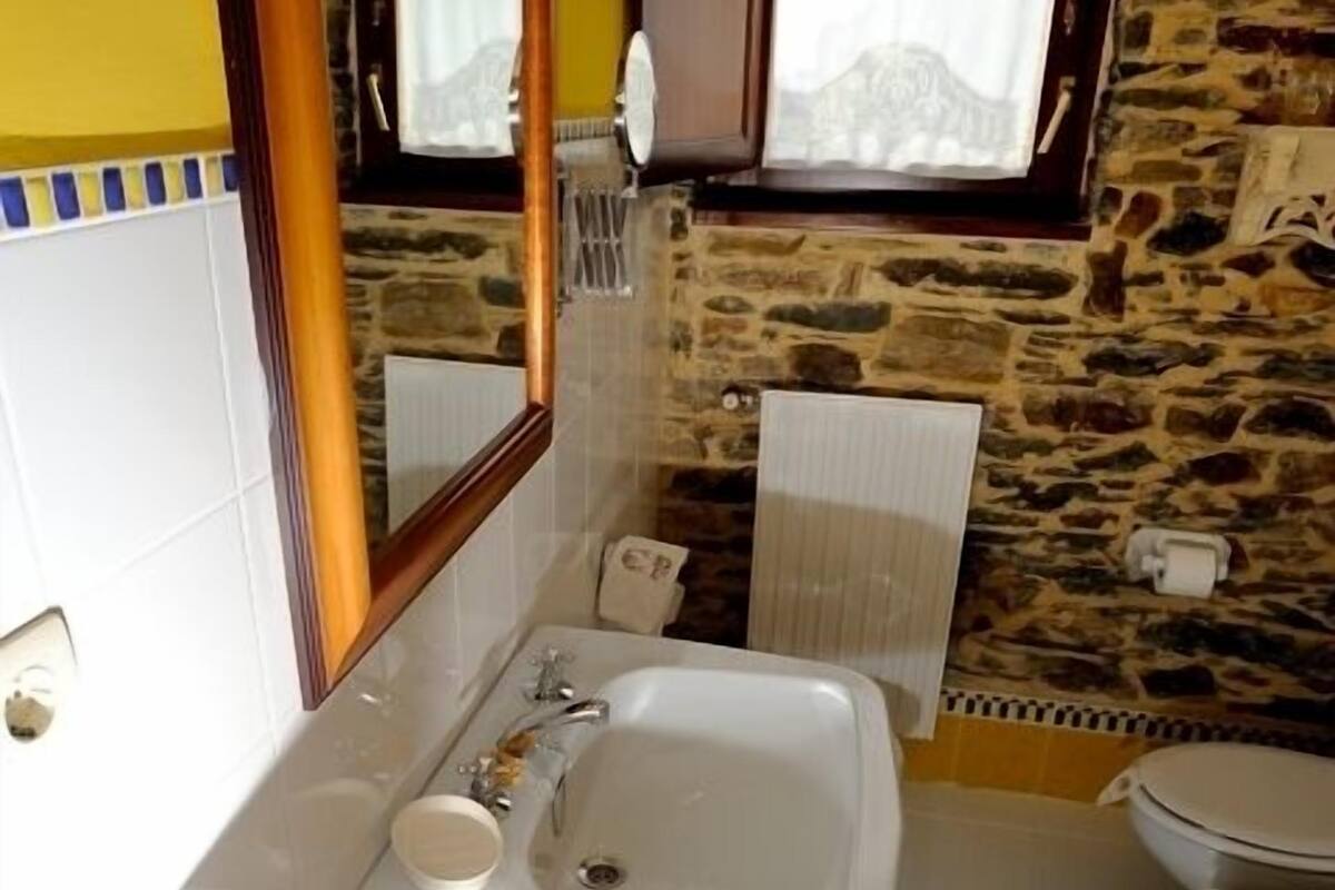 Ein Badezimmer mit einem weißen Waschbecken, einem Spiegel, einem Handtuchhalter und einem Fenster mit einer Steinwand.