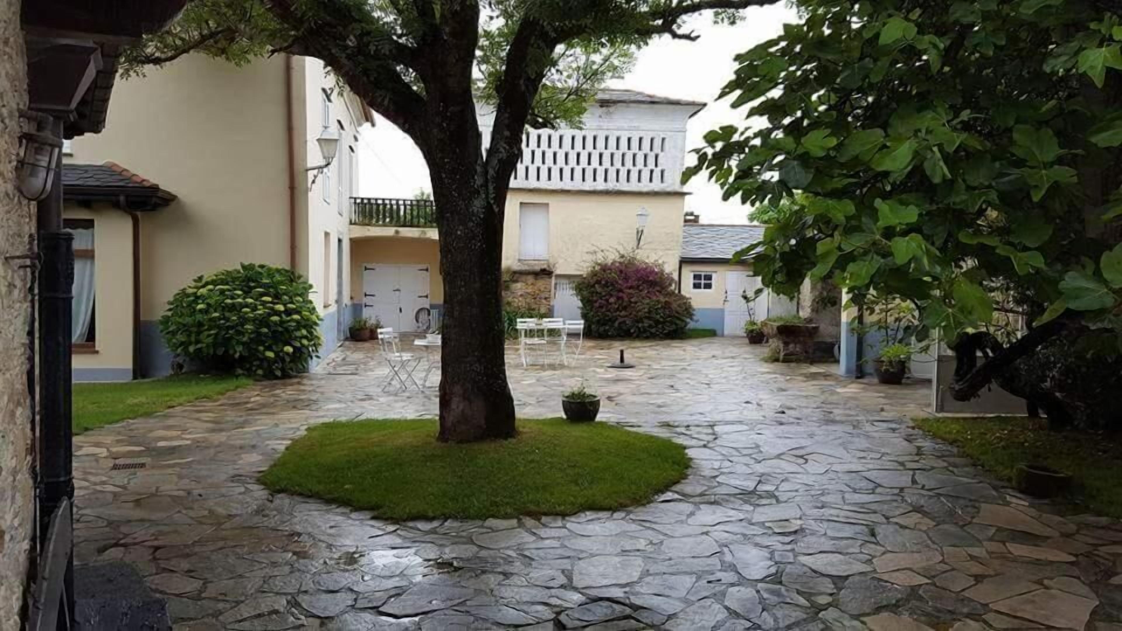 A courtyard with stone paving, a central tree, and surrounding greenery.