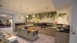 Un espace moderne dédié au petit-déjeuner, avec un buffet proposant une variété d’aliments, notamment une sélection de fruits.