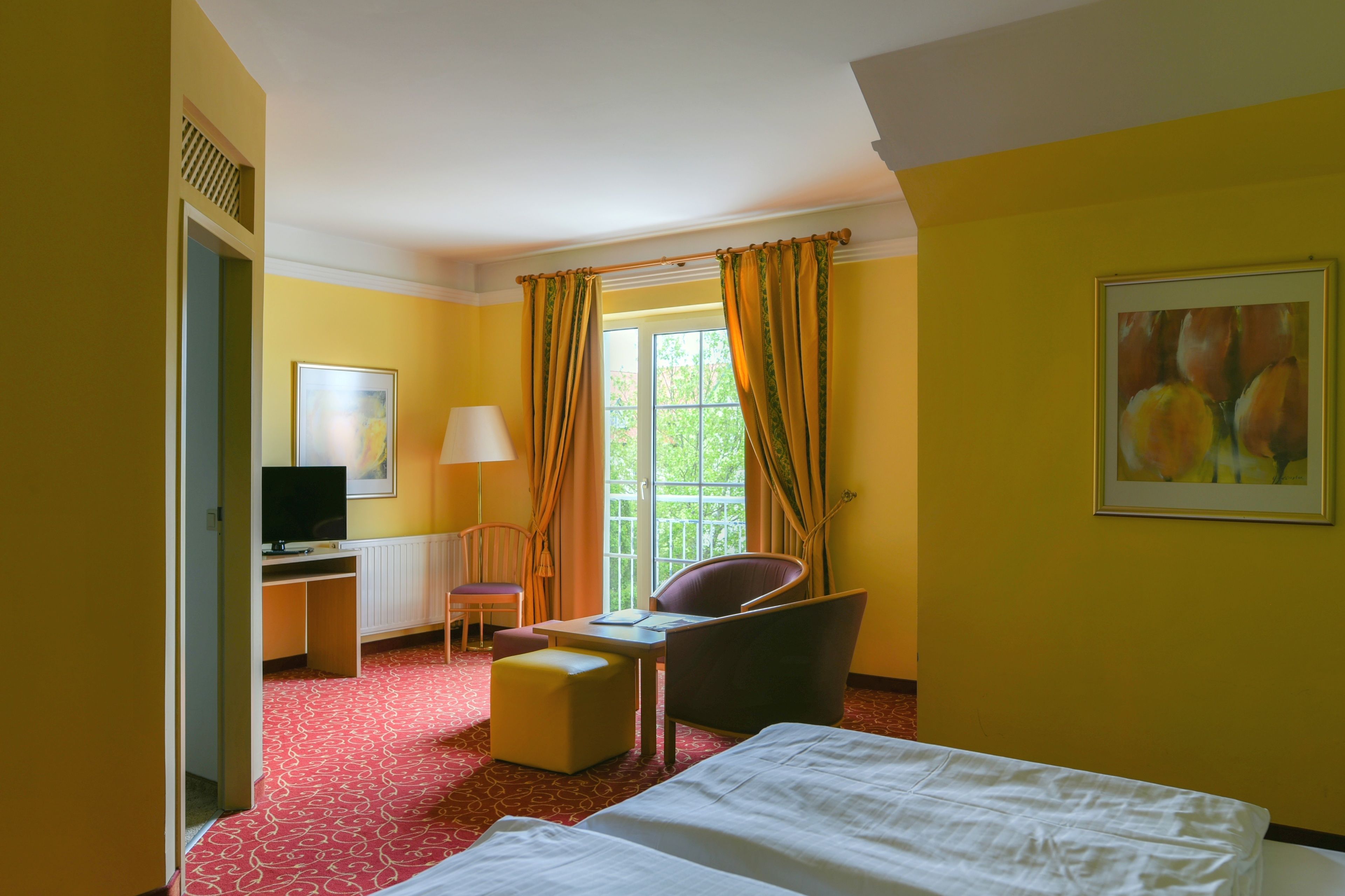 Una habitación de hotel con cama, escritorio, ordenador, silla, mesita y ventana con cortinas.