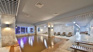 A large indoor swimming pool with benches, stone walls, and ceiling lights. - The Green Park Termal Sivas Hotels &Spa (Yildizeli)
