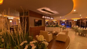 A modern hotel lobby with a curved seating area, a TV mounted on the wall, and a large window overlooking the pool area. - The Green Park Termal Sivas Hotels &Spa (Yildizeli)
