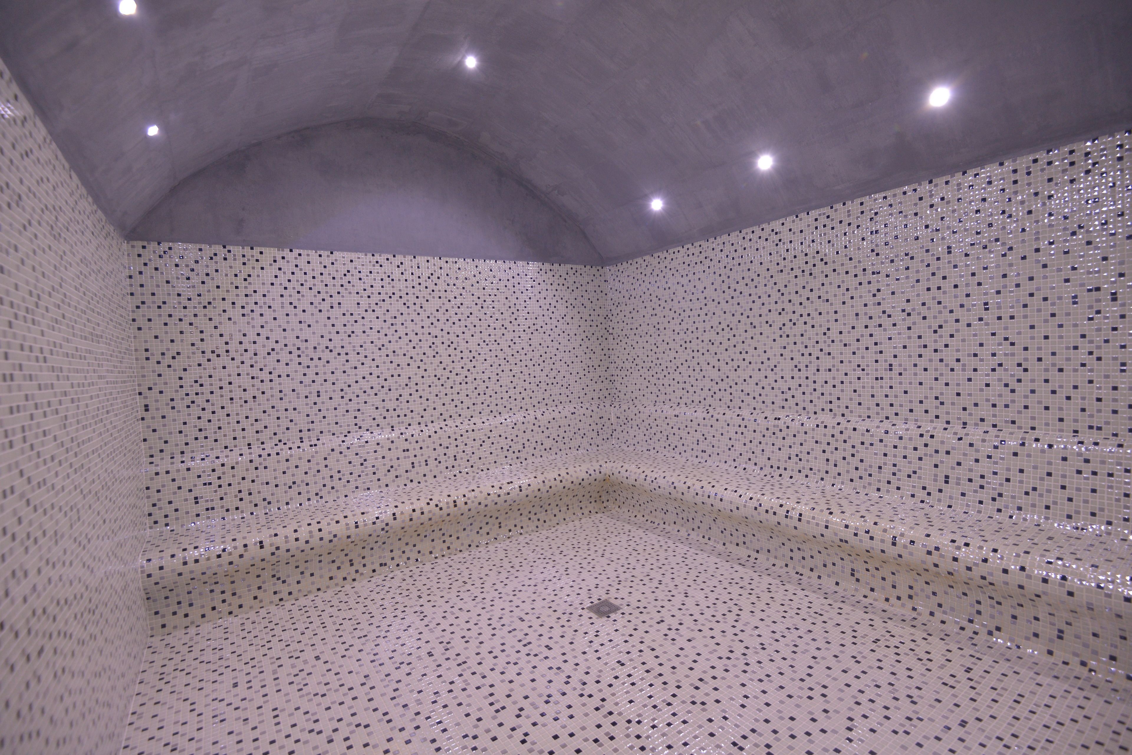 Una habitación con suelo y paredes de baldosas estampadas, techo curvo con iluminación empotrada y una lámpara central.