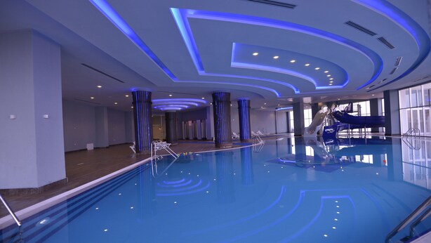 An indoor swimming pool with blue lighting, clear water, and a modern design. - The Green Park Termal Sivas Hotels &Spa (Yildizeli)