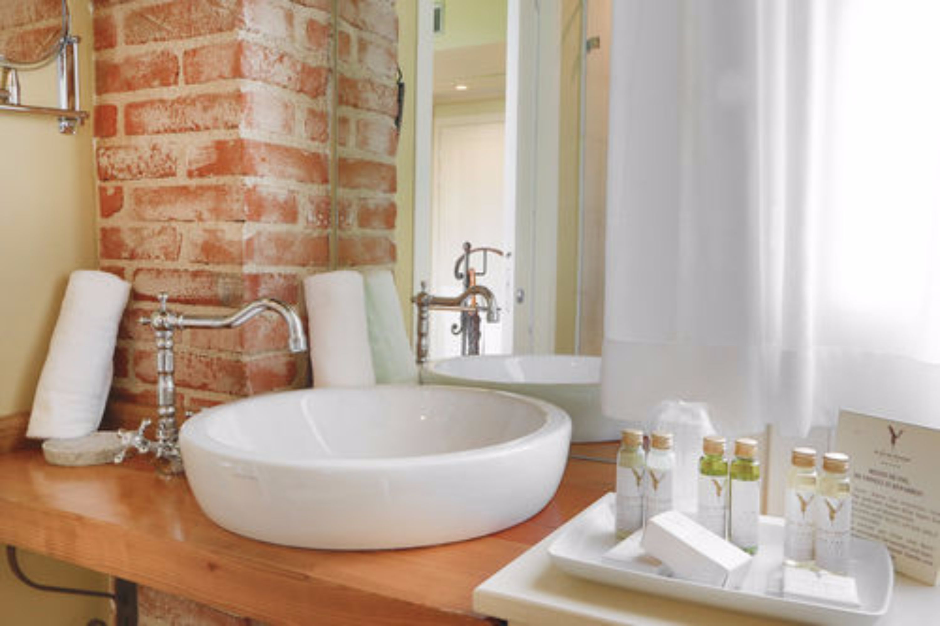 Un bagno con un lavandino bianco grande, una parete in mattoni, uno specchio e articoli da toilette sul ripiano.