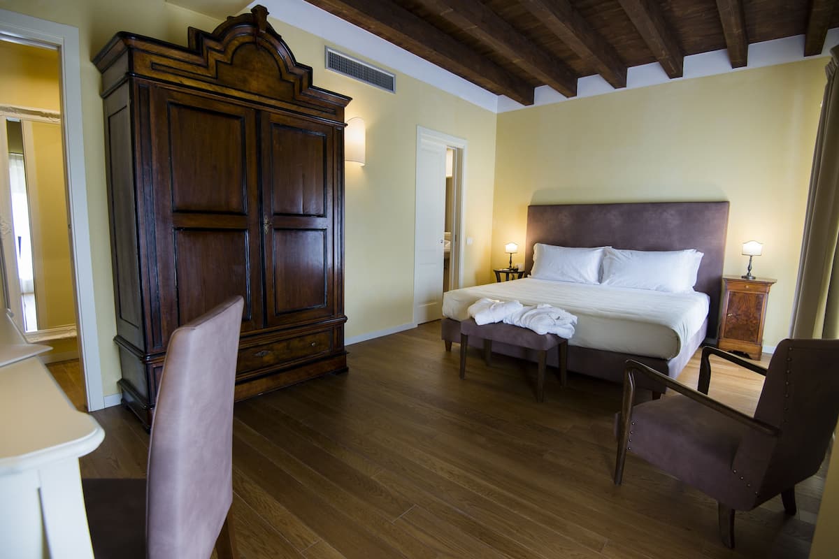 Un dormitorio con un amplio armario de madera, una cama con ropa blanca y dos mesitas de noche con lámparas.