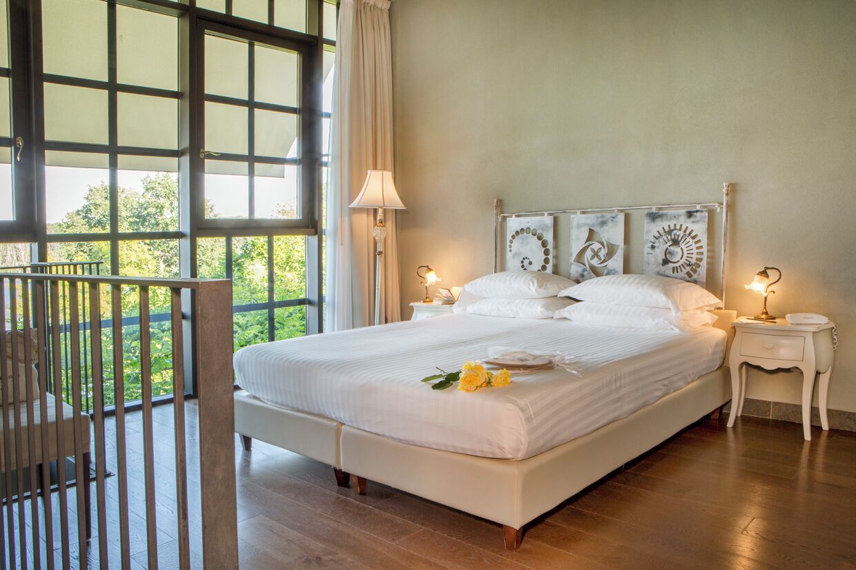A spacious bedroom with a large bed, two bedside tables, and a balcony with a railing.