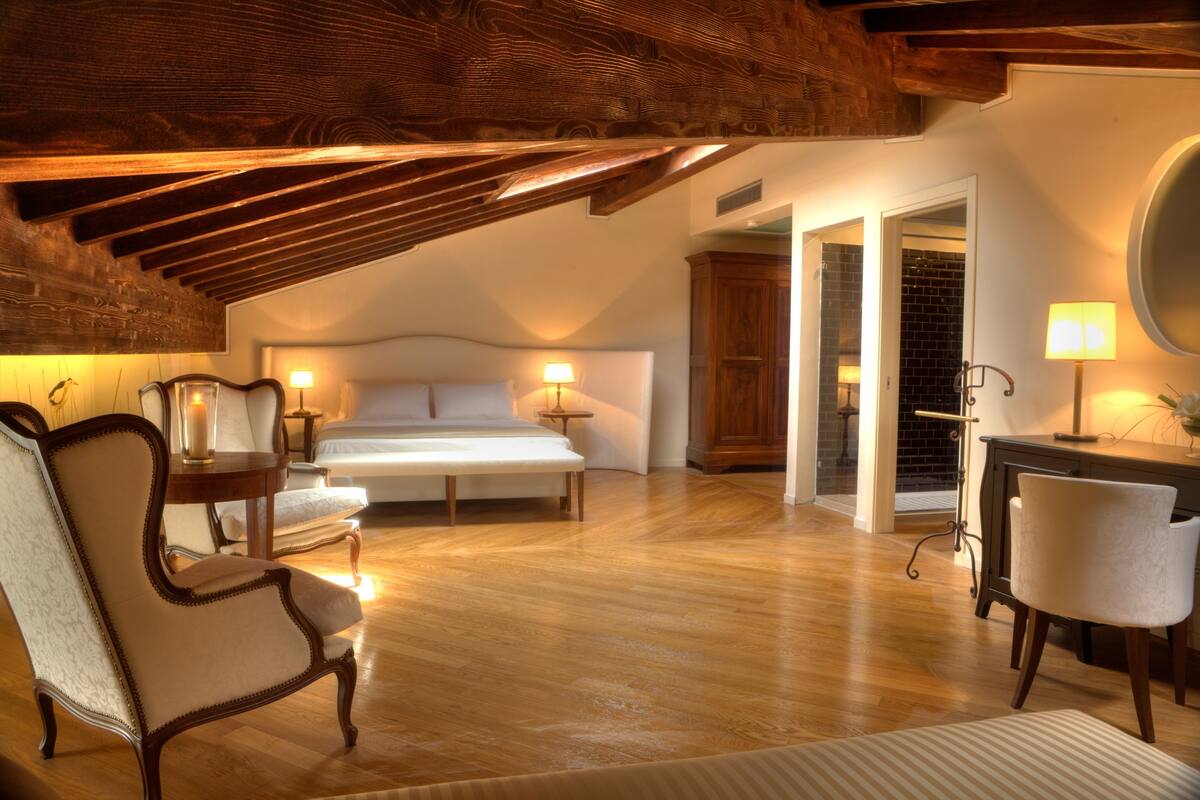 Un dormitorio estilo loft acogedor con techo inclinado, vigas de madera, una cama grande, un escritorio y una silla.