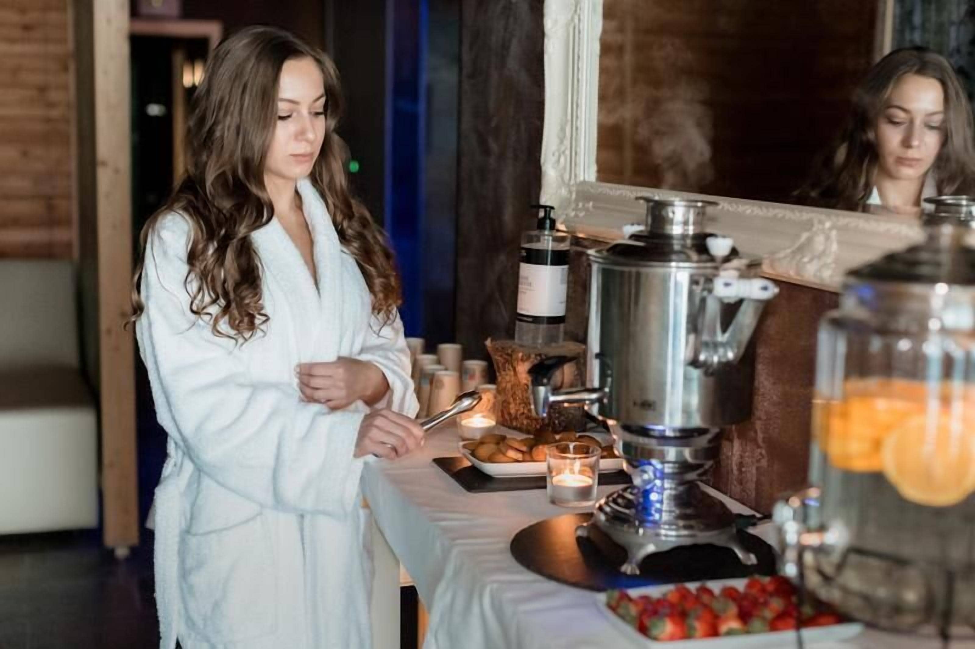 Una persona con una veste bianca prepara cibo a un tavolo con una macchina del caffè, candele e un piatto di frutta.