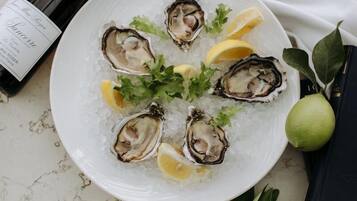 A plate of oysters on ice with lemon wedges and parsley, accompanied by a bottle of wine and a book.
