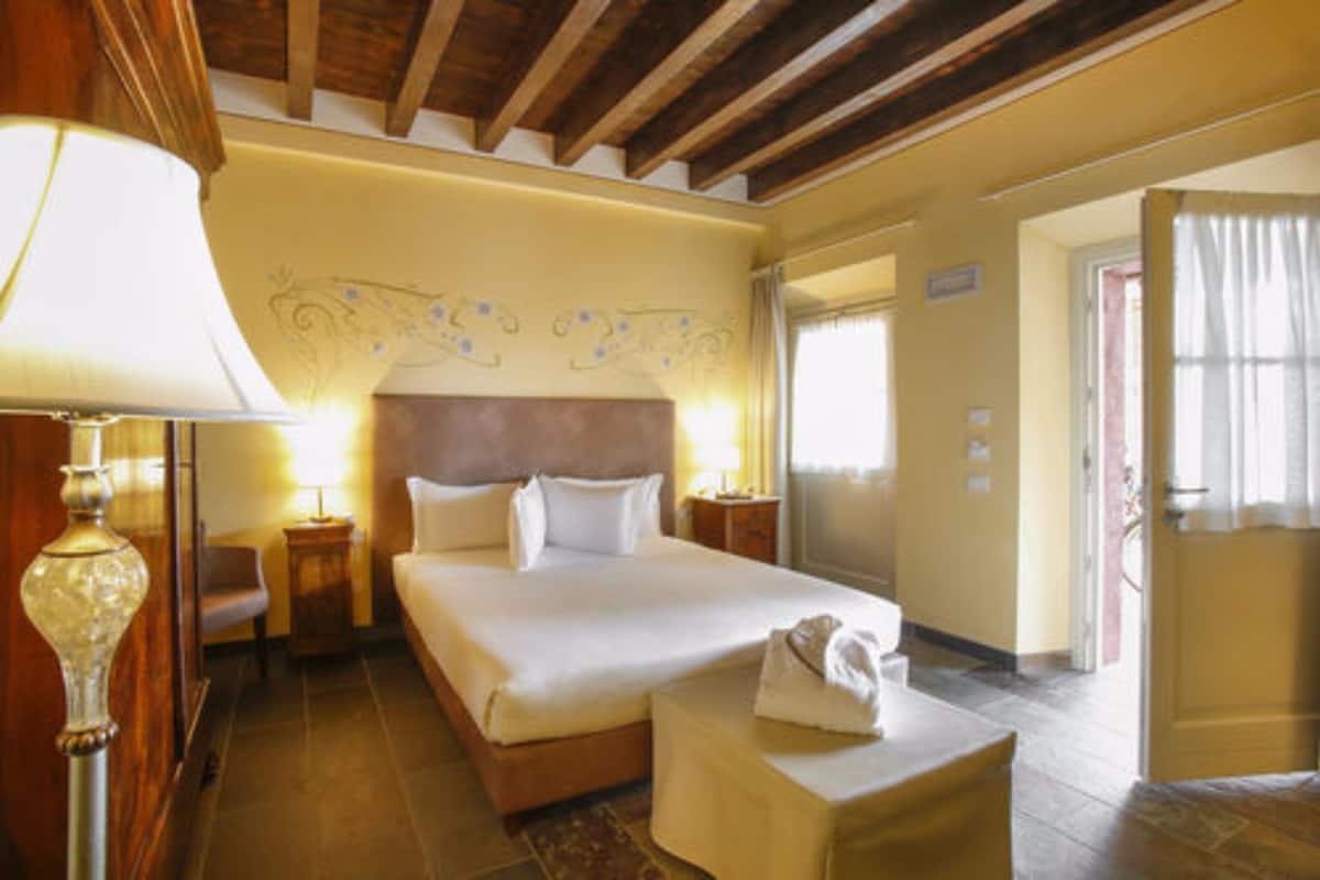 Habitación de hotel con una cama grande, mesitas de noche con lámparas, techo de madera y una puerta que da a otra habitación.