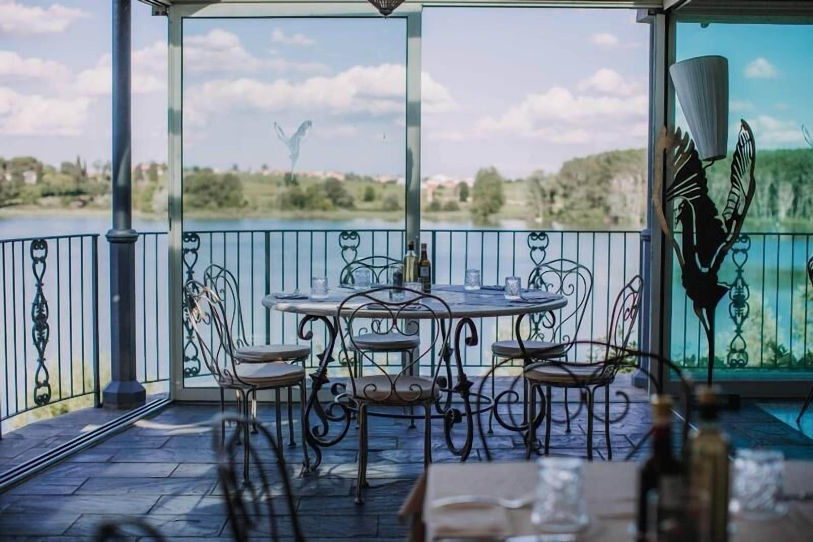 An outdoor patio with a round table and chairs, a view of a lake, and a decorative metal fence.