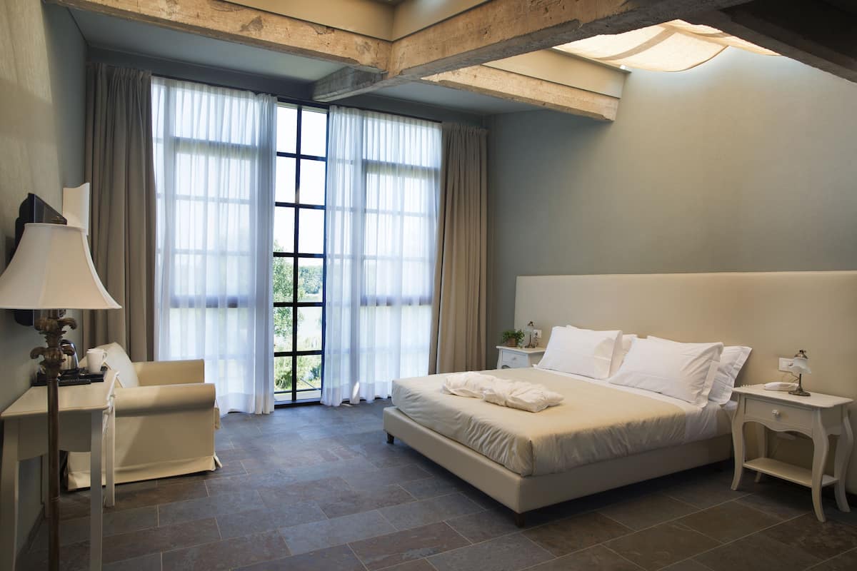 Un dormitorio con una cama grande, una silla, una mesita de noche y una ventana con cortinas.
