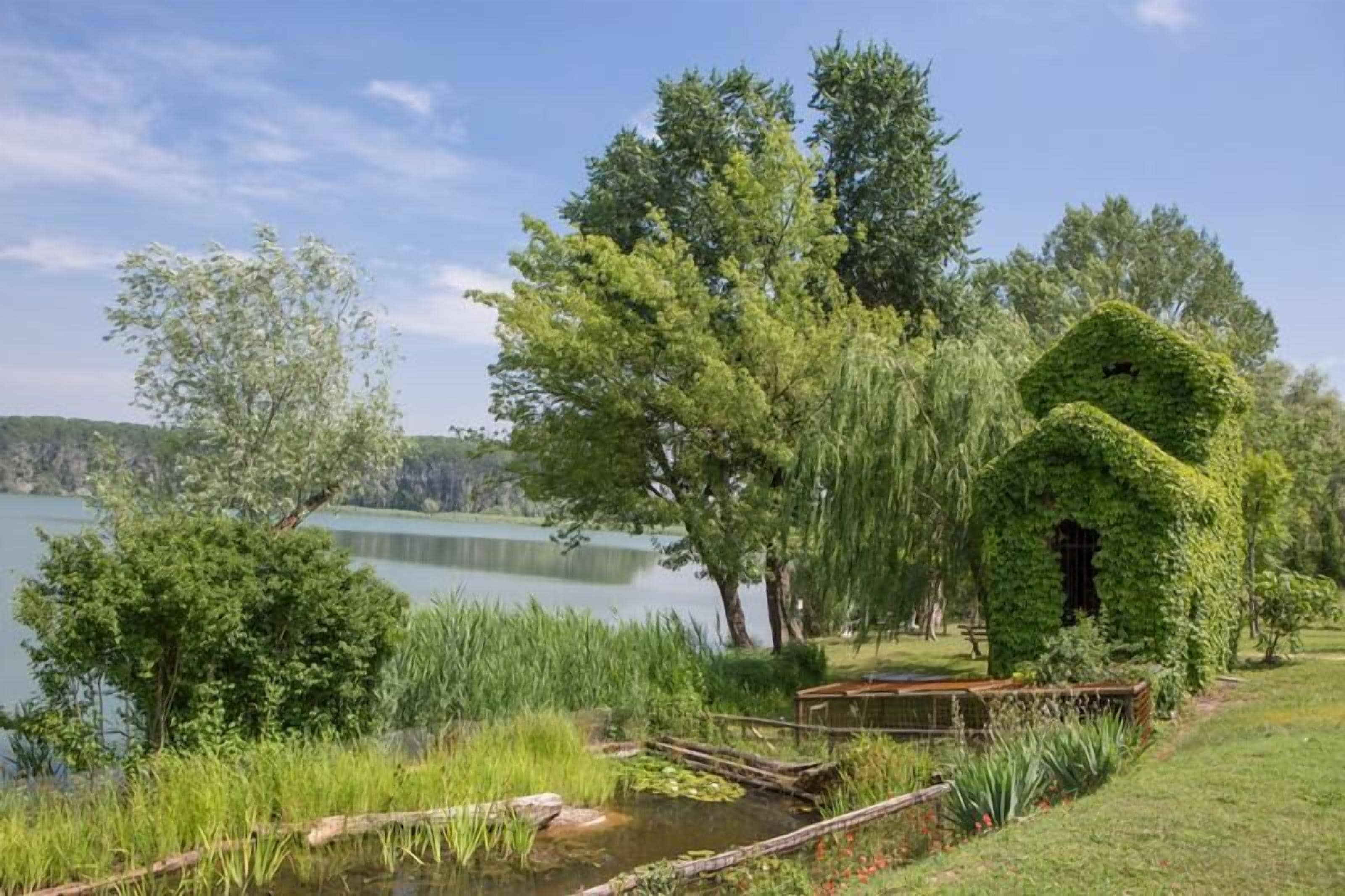 Un jardín tranquilo junto al lago con un pabellón, abundante vegetación y una superficie acuática serena.