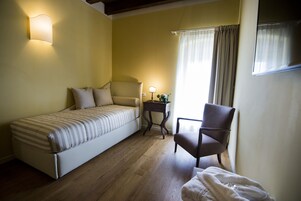 Un dormitorio con cama, una silla, una mesita de noche y una lámpara.