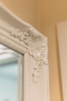 Un primer plano de un espejo con un marco blanco muy decorado y con detalles tallados.